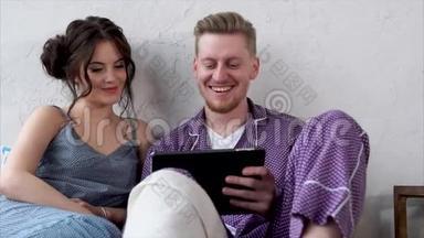 年轻夫妇躺在床上看平板电脑上的视频。