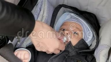 妈妈从一个躺在婴儿车里的孩子嘴里拿出一个奶嘴