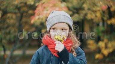 有趣的小女孩捧着一束小花，在令人惊叹的秋季公园慢动作中享受野花的芬芳