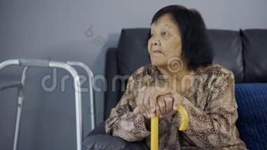 一位手持<strong>拐杖</strong>的老妇人坐在沙发上