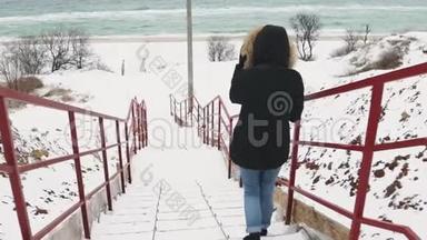 在寒冷的冬天，年轻漂亮的女人在海滩上走来走去。 慢动作