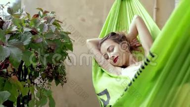 快乐的年轻女子轻松地躺在阳台上的吊床上。 女人在吊床上晒太阳