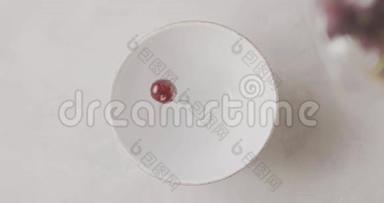 成熟的红色樱桃与水滴从一个白色的桌子上的玻璃容器掉进一个白色的陶瓷碗。 顶级