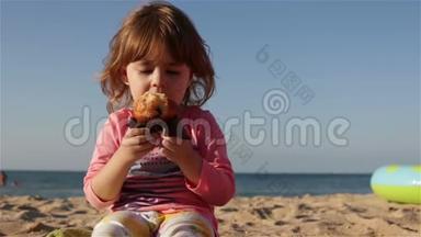 一个可爱的小孩子吃蛋糕，喝瓶子里的水。 她坐在沙滩上<strong>靠海</strong>