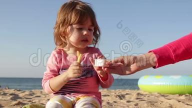 妈妈给女孩炸薯条和酱汁。 女孩坐在沙滩上的沙滩上靠在海边。