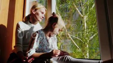 妈妈和女儿6岁，坐在窗台上，望着窗外。 窗外是春天，是绿色