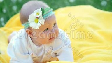 一个漂亮的小女孩，宝贝，<strong>躺在</strong>一个黄色的格子上，<strong>躺在草地</strong>上。 她的头上有一条用洋甘菊做的绷带。