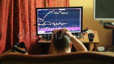 一个穿着T恤和短裤的男人，坐在沙发上的家里，监视着货币<strong>兑换</strong>时间表的变化