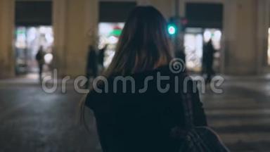 年轻的黑发女人在晚上穿过<strong>交通道路</strong>，独自走在市中心，穿过街道。