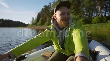 年轻的微笑快乐男子划船充气船与木桨在湖上。 高清慢动作生活方式录像。