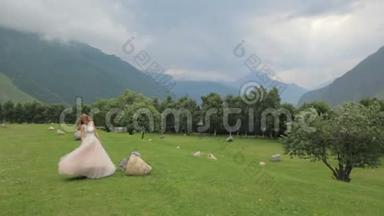 <strong>红</strong>发新娘穿着<strong>奢华</strong>的礼服，在高山的映衬下，沿着绿草地散步。 婚礼日