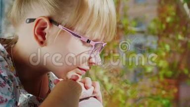 金发女孩6岁戴着粉红色眼镜<strong>看</strong>着<strong>窗外</strong>。 <strong>窗外</strong>，春天，听到一棵树的绿叶