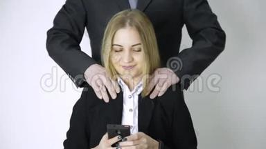 女商人在手机上自拍，雇员在做了很长时间的工作后，会按摩她的肩膀和脖子