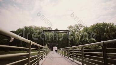 刚结婚。 一位新娘和一位穿着结婚礼服的新郎在夏天牵着手走在桥上。