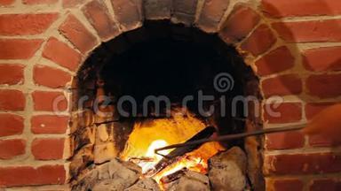 一个人在烧砖的壁炉里用耙子搬木头