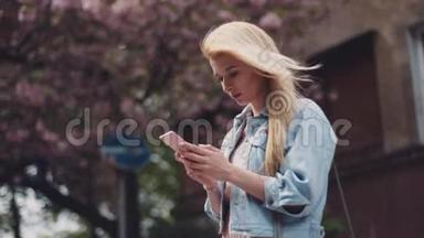 城市里的<strong>风天</strong>气。 年轻的女人在用她的手机。 背景上的樱桃开花和路标