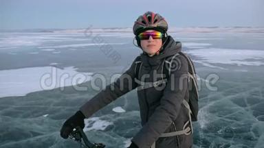 人是站在冰上的自行车。 他看着美丽的日落。 骑自行车的人穿着灰色的羽绒服，背包