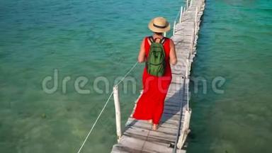 穿着红色长裙走在码头上的美女。 Phu Quoc岛。 女人在木墩上背着背包