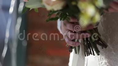 身着白色婚纱的年轻新娘手中捧着美丽的新娘花束。 新娘手触摸婚礼花束