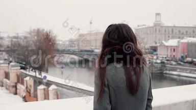 后景。 站在桥上悲伤的黑发女孩叹了口气，看着白雪覆盖的冬季小镇。