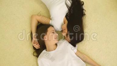 母亲和女儿穿着粉红色睡衣躺在床上，微笑着的母亲，女儿笑着，俯视着