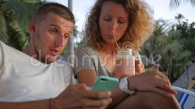 年轻夫妇在素食咖啡厅喝健康的冰沙，在手机上观看照片。 高清慢速运动。 Phanganan