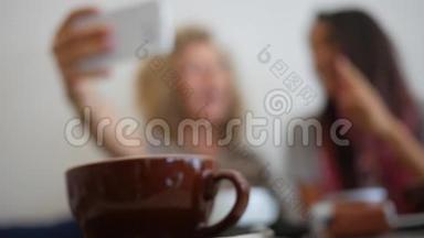 年轻女孩坐在咖啡厅，在<strong>手机</strong>上<strong>制作</strong>照片自拍。 咖啡杯近景与背景人士