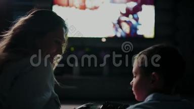 妈妈带着儿子在电视前玩电子游戏，互相传递操纵杆。 电视屏幕的后视图。