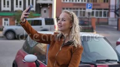年轻快乐的女人在街上的智能手机上拍新照片。 在路上为社交网络做自拍的女孩