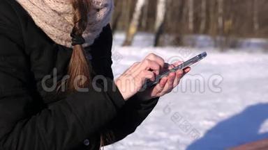 冬季晴天智能手机上的妇女浏览图片、文字、号码