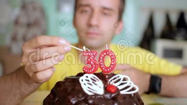 一个男人用蝴蝶翅膀在巧克力蛋糕上点燃30年的蜡烛。 这个人今天过生日。