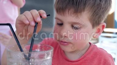 男孩在舒适的街头咖啡馆里坐在桌上，用玻璃吸管喝饮料，美丽的孩子做零食