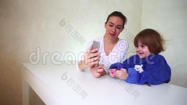 年轻的母亲和小女儿玩手机相机，女孩坐着，使用有趣的相机效果。