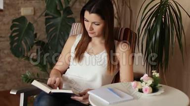 年轻漂亮的女人看书和做笔记。 坐在椅子上看书的女人。