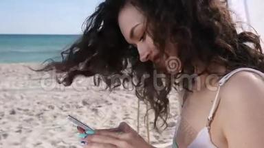女孩在海滩上的社交网络中交谈，微笑的女人在海洋海岸使用手机，年轻的女人在手机上查看资料。