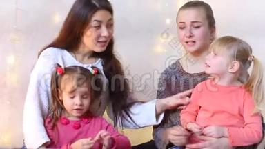 两位妈妈带着小女儿<strong>坐在地板上</strong>，通过视频交流与亲戚交谈。