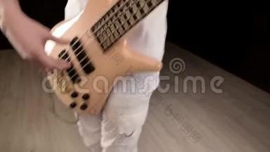 年轻的男音乐家穿着白色的衣服，黑色背景上有一把米色的低音吉他。 低音吉他演奏者演奏音乐
