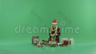 一个年轻的女人正坐在绿色的屏幕上打开她<strong>身边</strong>的空圣诞礼物