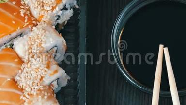 摄像机向右移动。 在酱油和中国竹签旁边的黑色木制背景上摆放时尚寿司