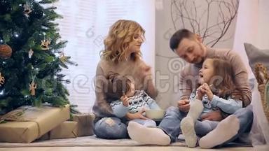 圣诞快乐，<strong>一家人</strong>穿着毛衣，爸爸妈妈和两个<strong>女儿</strong>坐在树下，笑着互相买东西