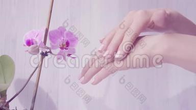 嫩女人手的特写镜头涂抹护肤霜.. 紫色兰花的光背景。 美丽的双手优雅