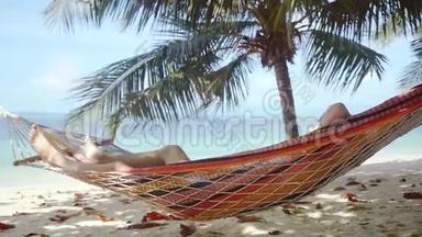 年轻人在热带海滩的吊床上放松。 在棕榈树旁边的吊床上睡觉的人。 慢动作。 1920x1080