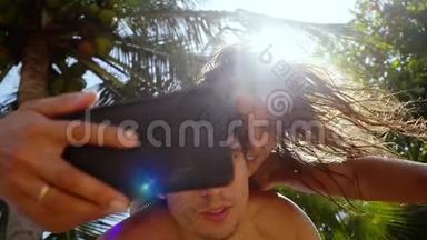 快乐夫妇在智能手机上拍自<strong>拍照片</strong>，在棕榈树下和背景上的太阳。 <strong>女人</strong>在炫耀
