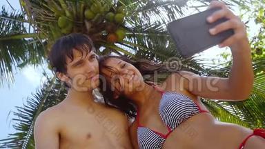浪漫的幸福的情侣在阳光下，在户外的棕榈树下，在手机上自拍，在阳光下和