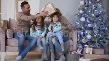 <strong>圣诞节</strong>快乐的<strong>一家人</strong>，妈妈，爸爸和两个小女孩坐在家中的沙发上靠近圣诞树，打开