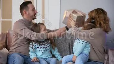 圣诞节快乐的一家人，妈妈，爸爸和两个小女孩坐在家中的沙发上靠近圣诞树，打开