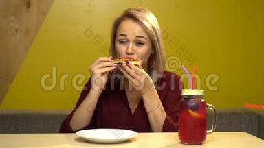 漂亮的金发女孩在咖啡馆里吃比萨饼，<strong>胃口</strong>很好。 桌子上有一罐柠檬汁