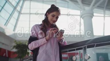 可爱的年轻女孩与漂亮的化妆在粉红色衬衫是集中在她的智能手机，她正在玩一个应用程序。