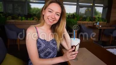 快乐的女孩坐在咖啡馆里喝着冰淇淋鸡尾酒，慢<strong>悠悠</strong>地看着镜头。
