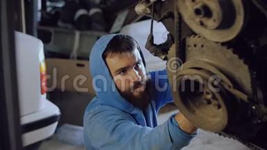 有胡子的汽车机械师坐着，从下面的螺丝螺栓进入电机的身体挂在链条上。